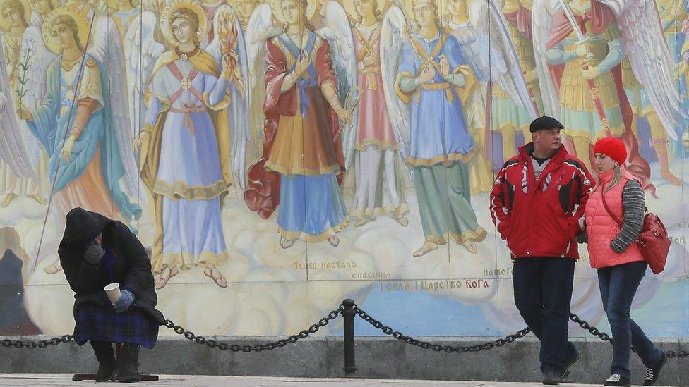 An old Ukrainian woman begs for money in front of Mikhailovskiy Cathedral frescos in downtown Kiev