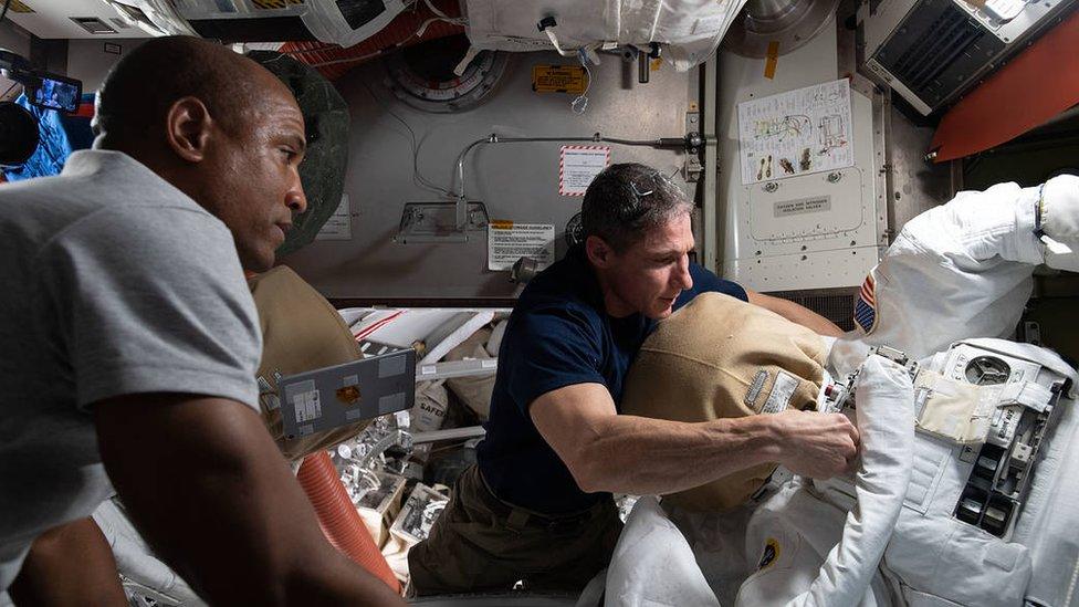 NASA astronauts Victor Glover (left) and Michael Hopkins (right) work on U.S. spacesuit maintenance inside the International Space Station's Quest airlock.