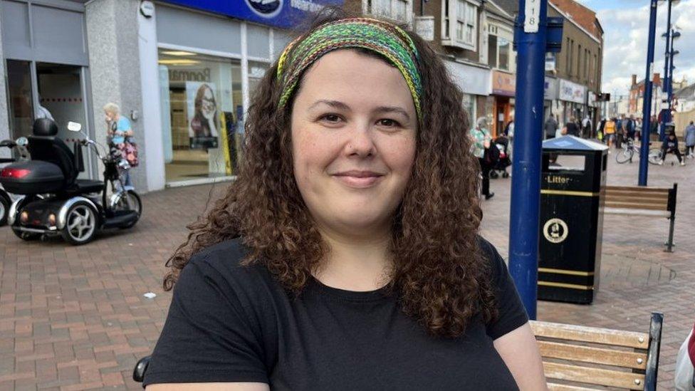 A woman with brown hair and a colourful headband smiles at the camera