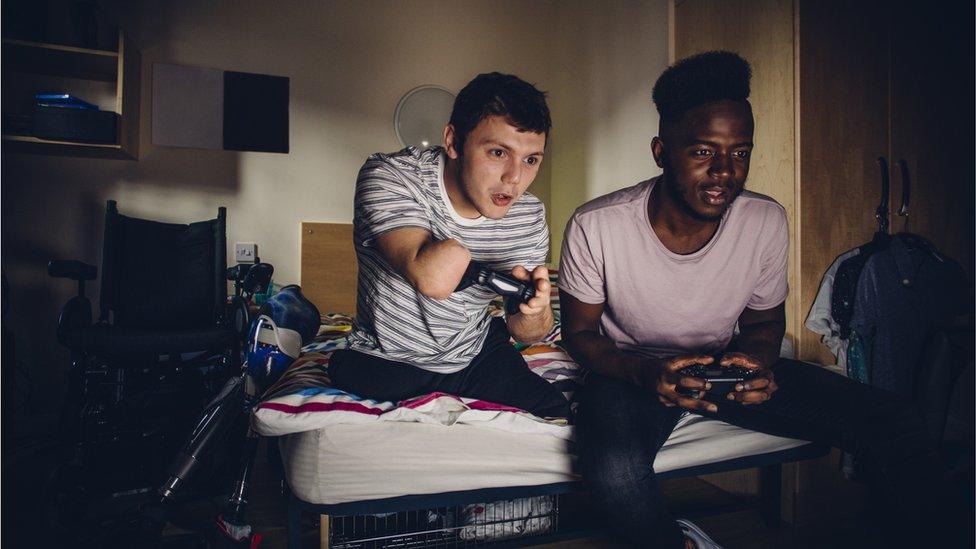 two boys game together - one boy uses his controller in an adapted way as he does not have a hand