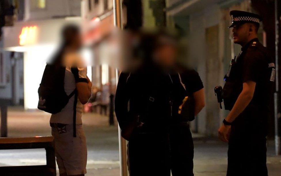 Teenagers with blurred out faces talking to police officers in a street in Ipswich at night