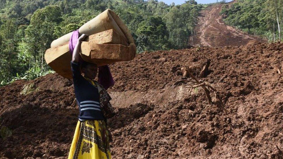 A woman carries a rolled-up mattress at a landslide site in Shisakali village of Bududa district, eastern Uganda,