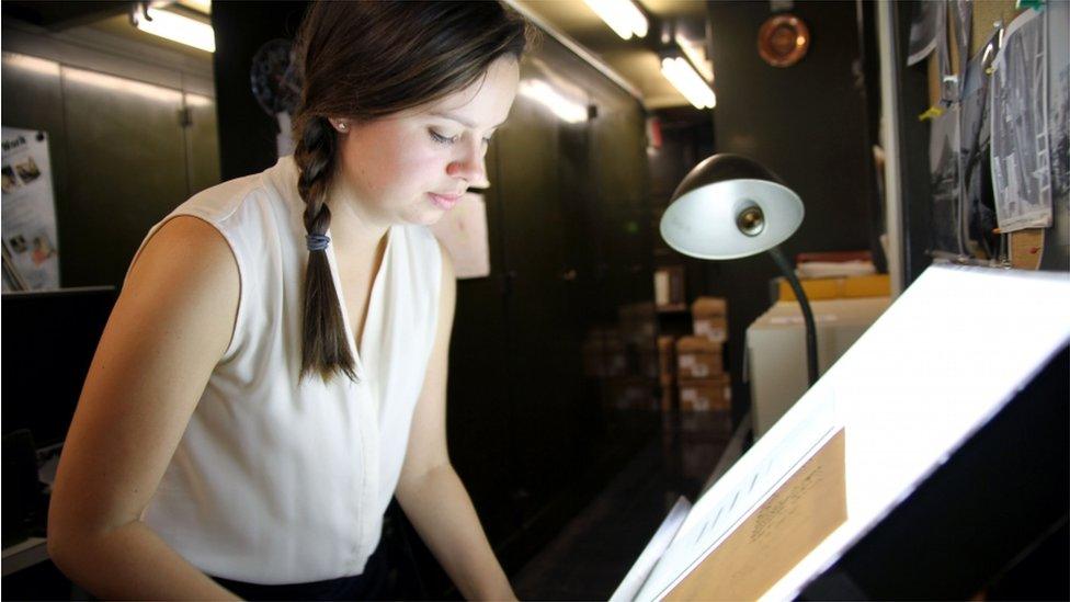 Curator Lindsay Smith Zrull places a glass plate photograph of a section of the sky onto a lightbox