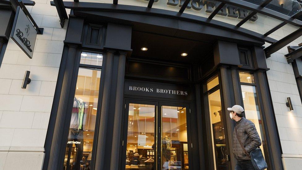 person in mask walks by Brooks Brothers store