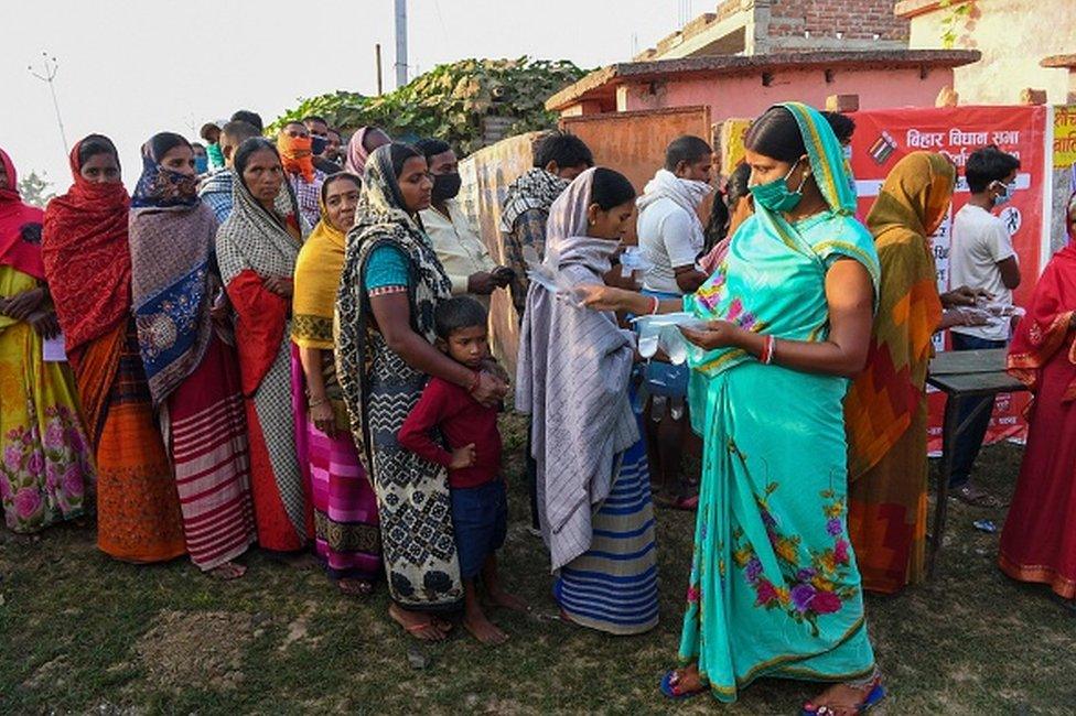 An electoral official (R) distributes plastic hand gloves to voters waiting to cast their ballots for Bihar state assembly elections at a polling station in Patna on October 28, 2020. (