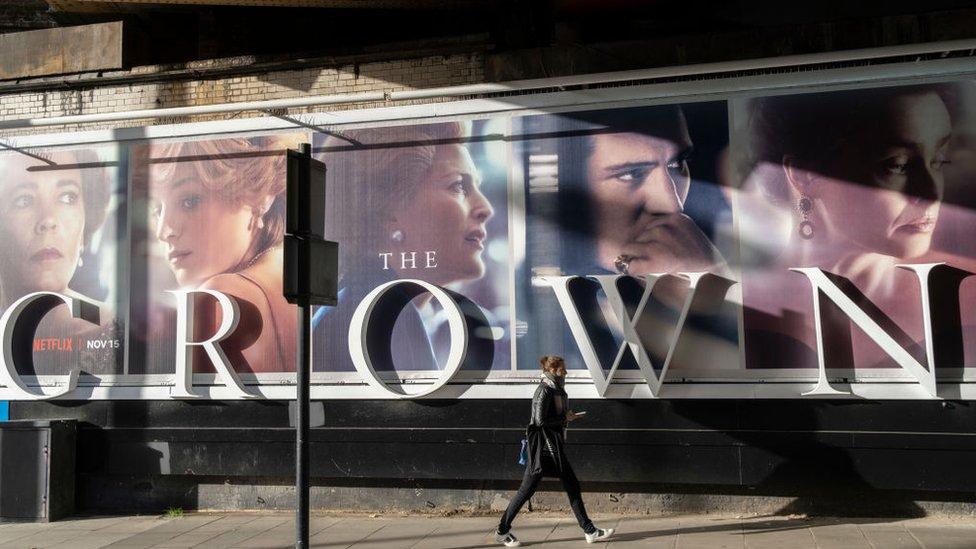 A woman walks in front of a billboard for The Crown