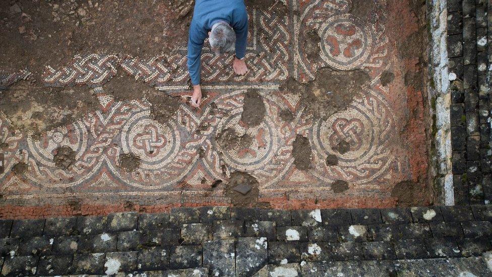 a mosaic being uncovered by a man in a blue shirt