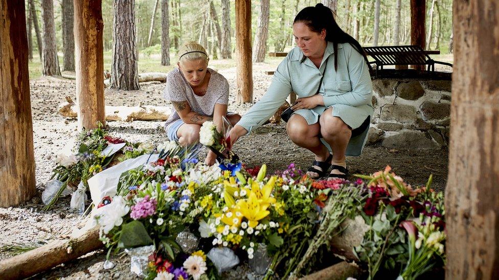 People lay flower bouquets as a makeshift memorial at a forest shelter next to the Haslevej road near Roenne, Bornholm island, Denmark