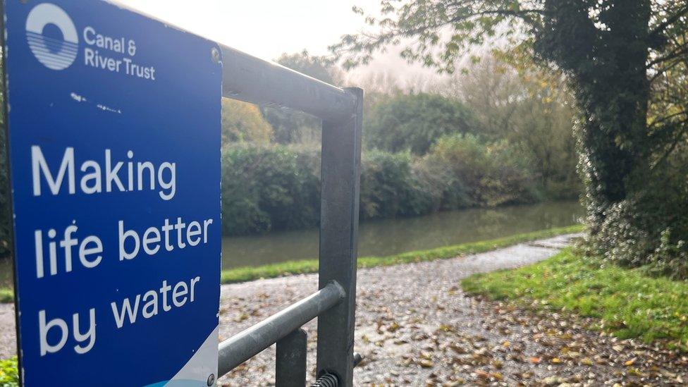 Gate with a canal and river trust sign on it that reads "making life better by water"