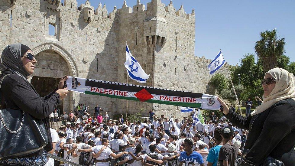 Palestinian women hold Palestine scarf as Israelis