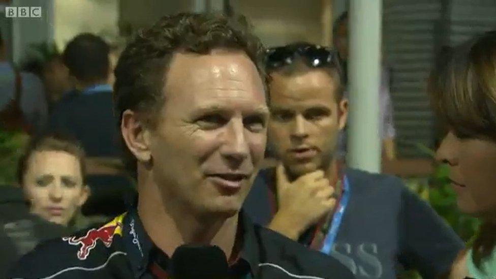 Man with short hair in racing clothes speaks into a microphone at a Grand Prix