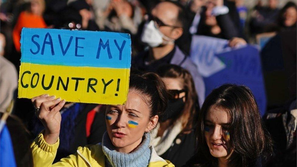 Ukrainian holds up a sign saying "Save my country"