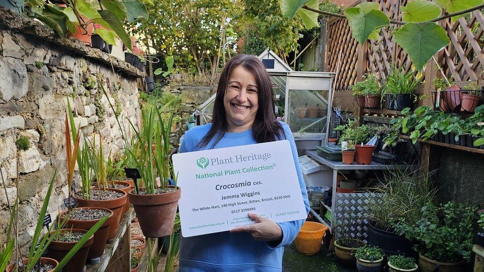 Jemma Wiggins holds up a certificate as she stands in her pub garden at the White Hart at Bitton