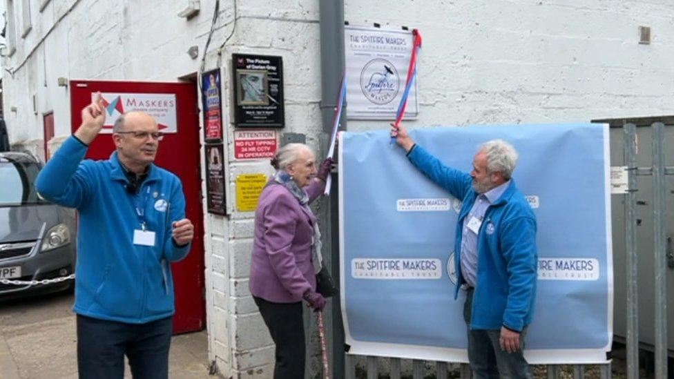 Three people unveiling a plaque