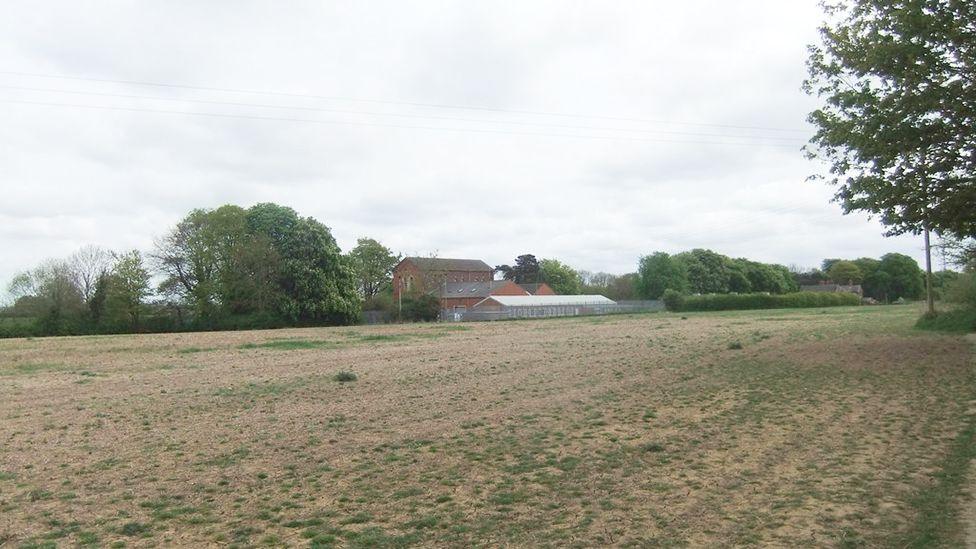 A view of the land where the wood will be created which is now a scrubby field with the brick pumping plant building in the background