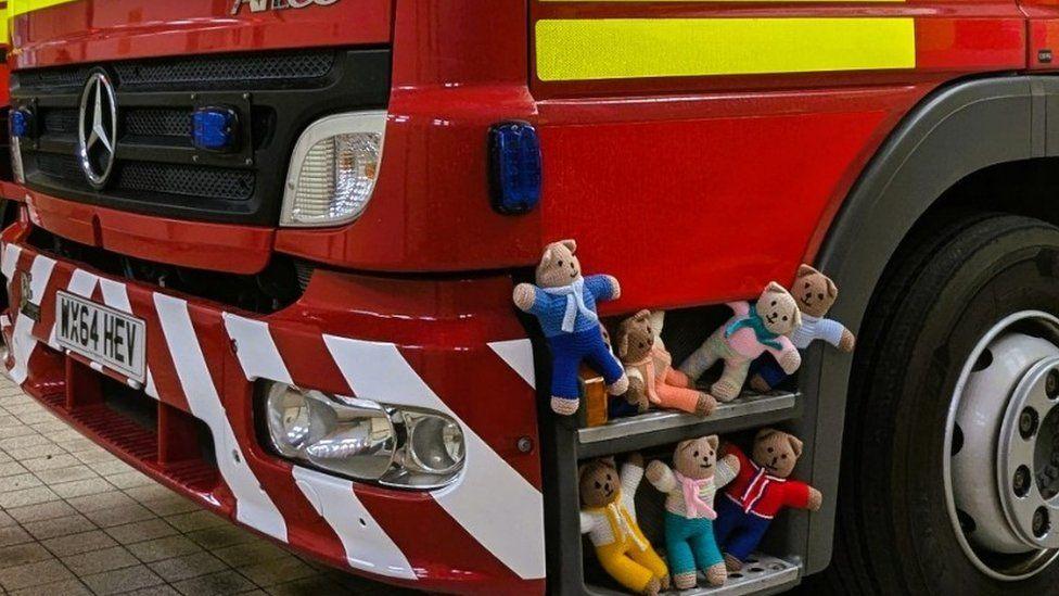 Teddy bears set on two steps of a fire engine - four on the top step and three on the lower step