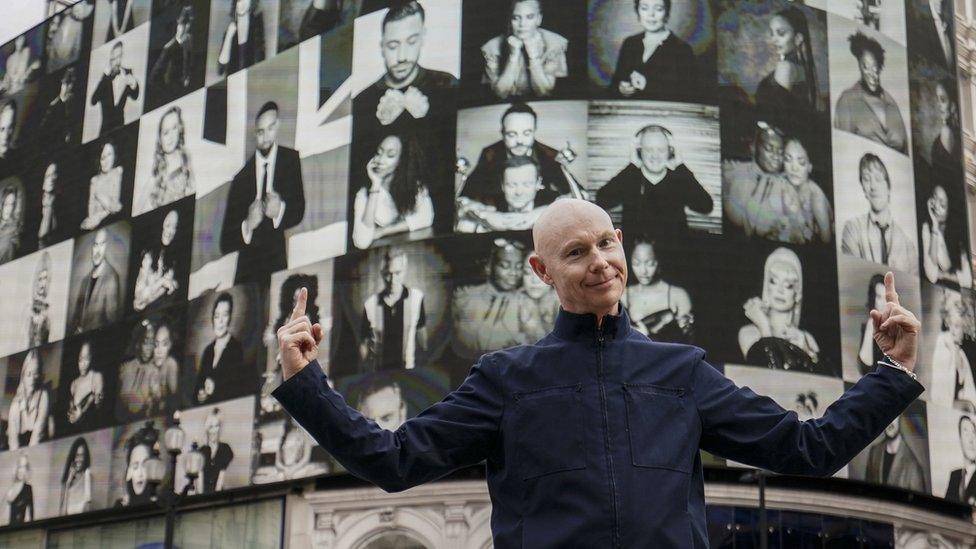 A man holding his hands up with the backdrop of an exhibition.