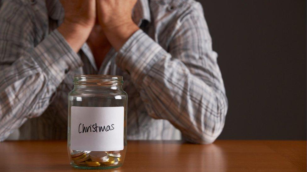 A man with his head in his hands looking at a jar of money labelled Christmas