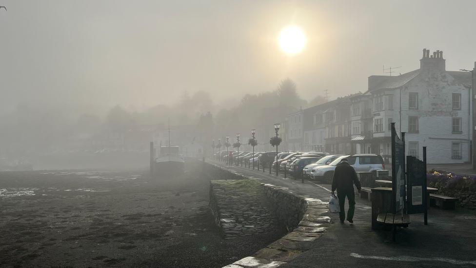 Misty morning in Tarbert, with a man walking along the harbour