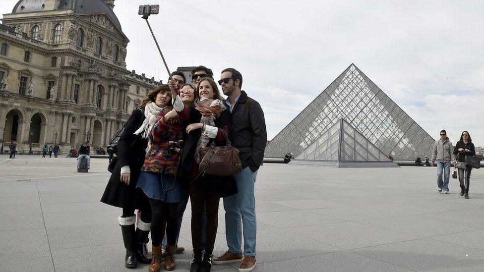 Tourists use a selfie stick outside the Louvre