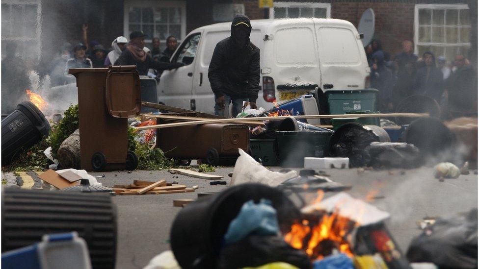 A man with a hood up stands behind a makeshift road block