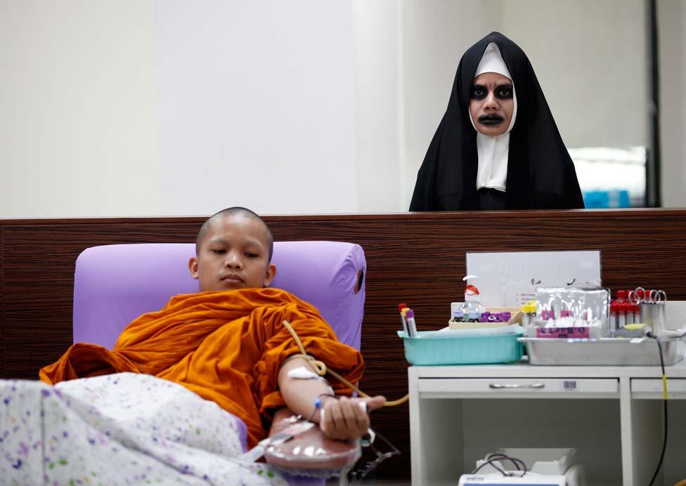 A Buddhist monk donates blood next to a staff member dressed in a nun horror costume during a Halloween blood donation drive at the National Blood Center of the Thai Red Cross Society in Bangkok, Thailand