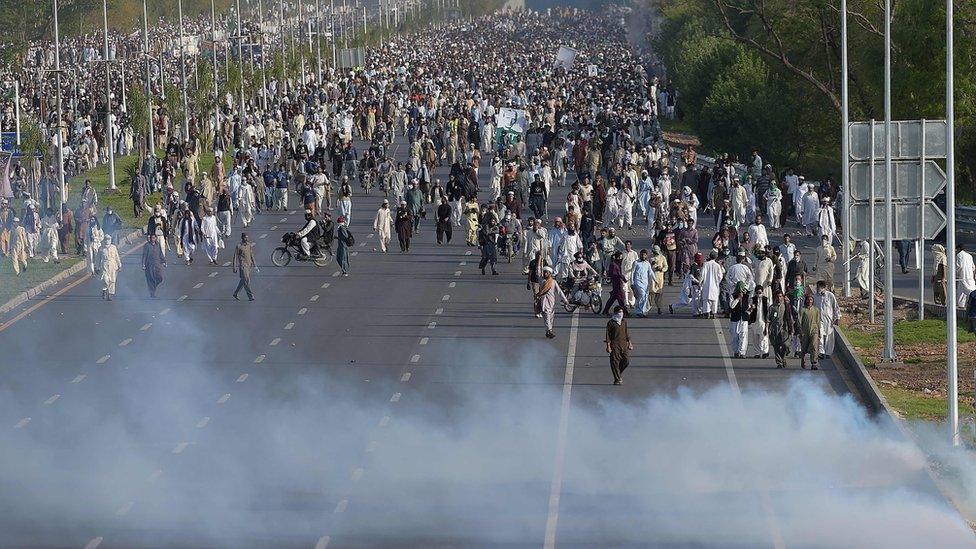 Supporters of executed Islamist Mumtaz Qadri walk through tear gas fired by police officers