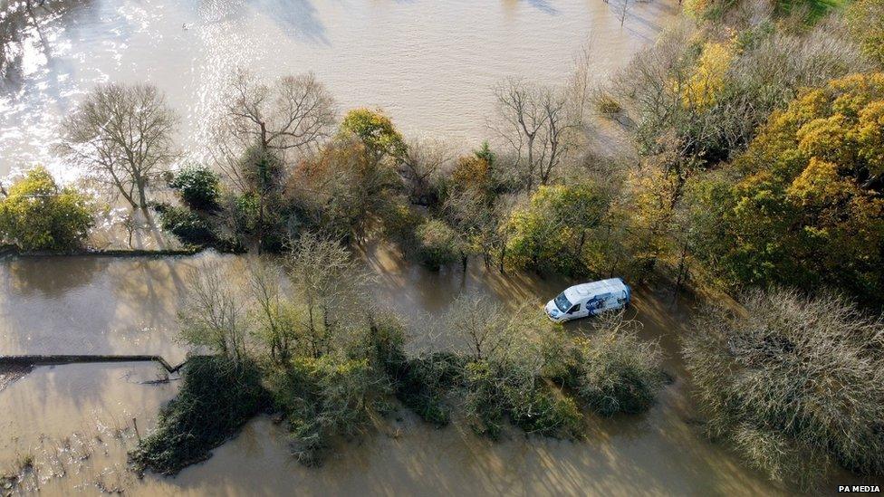 A van is trapped in floodwater that has surrounded a road and trees