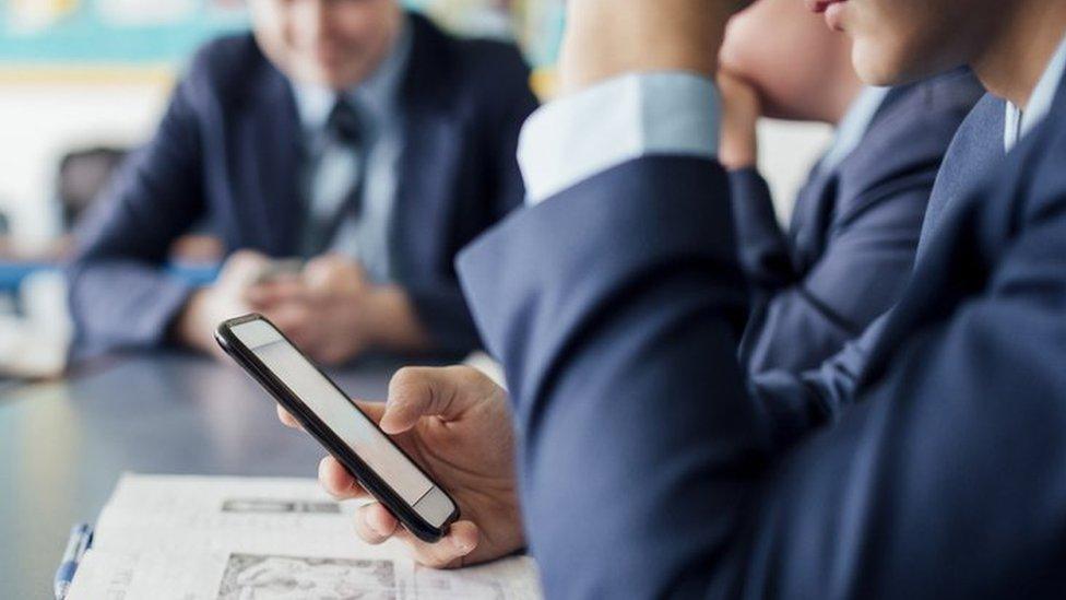 A school pupil in uniform using a smartphone at their desk