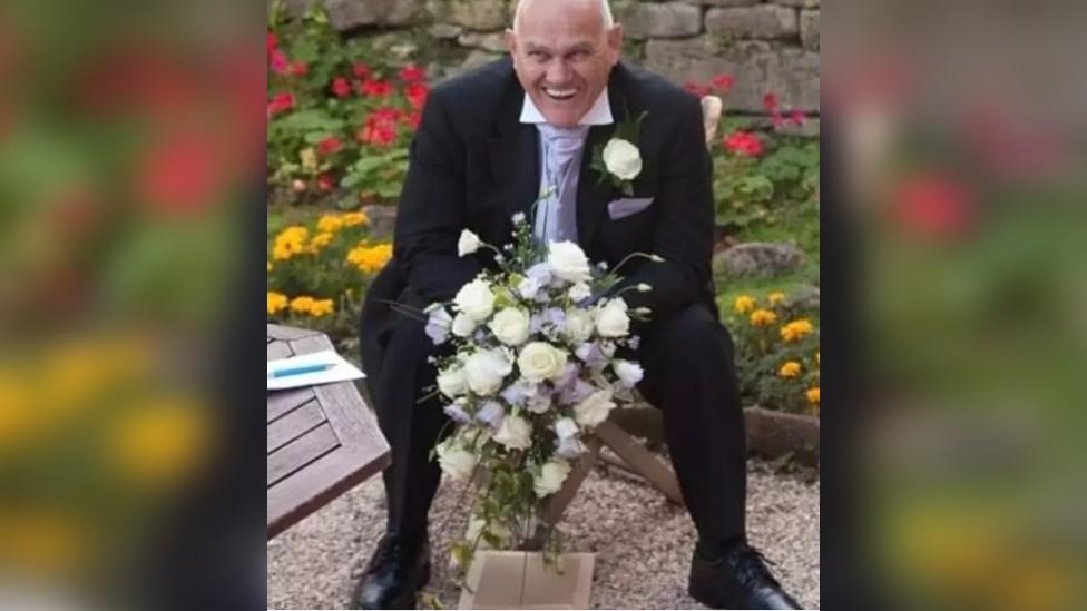 Richard Reeves smiling holding a bunch of white flowers