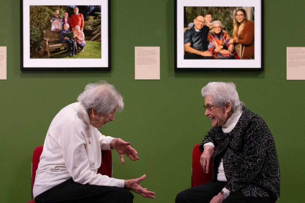 Holocaust survivors Marianne Philipps (L) and Anne Super (R) sit beneath portraits of themselves