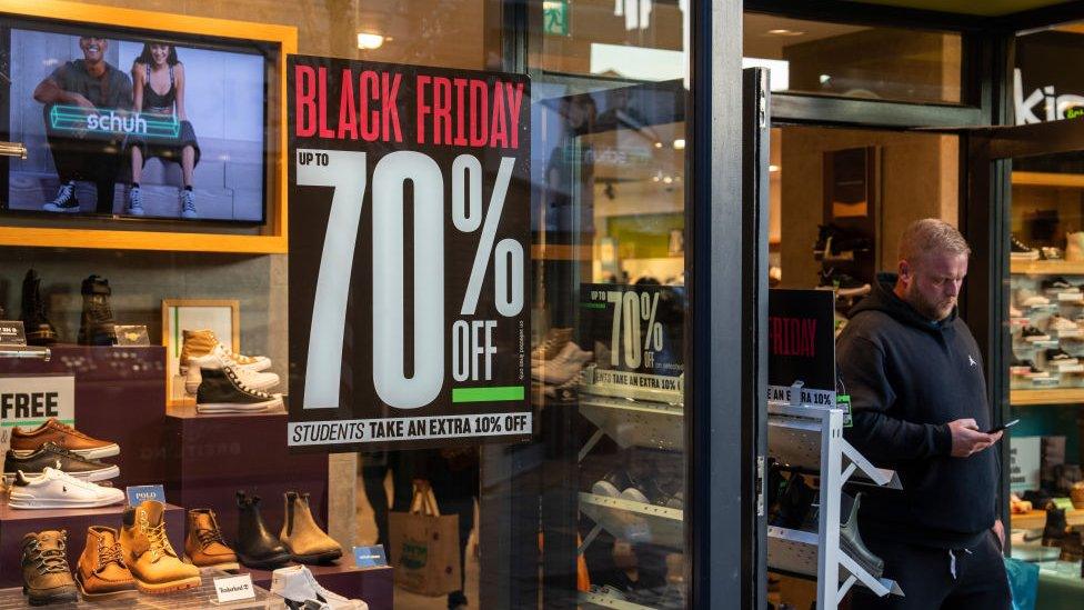 a man walks out of a shop that has a black friday deal on display