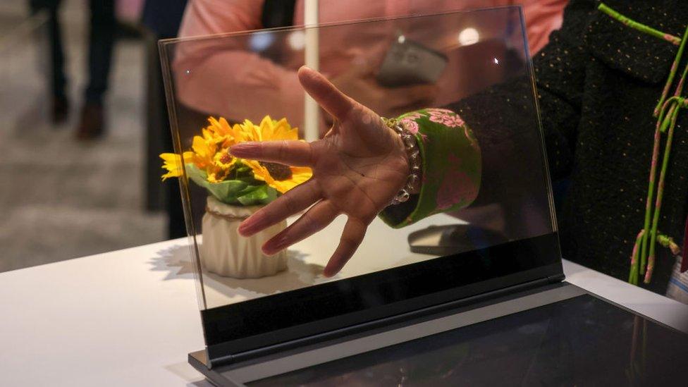 a person holds their hand behind a transparent laptop display