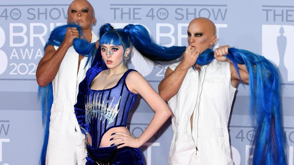 Photo of Ashnikko at the Brit Awards with her hair being carried by two faceless men