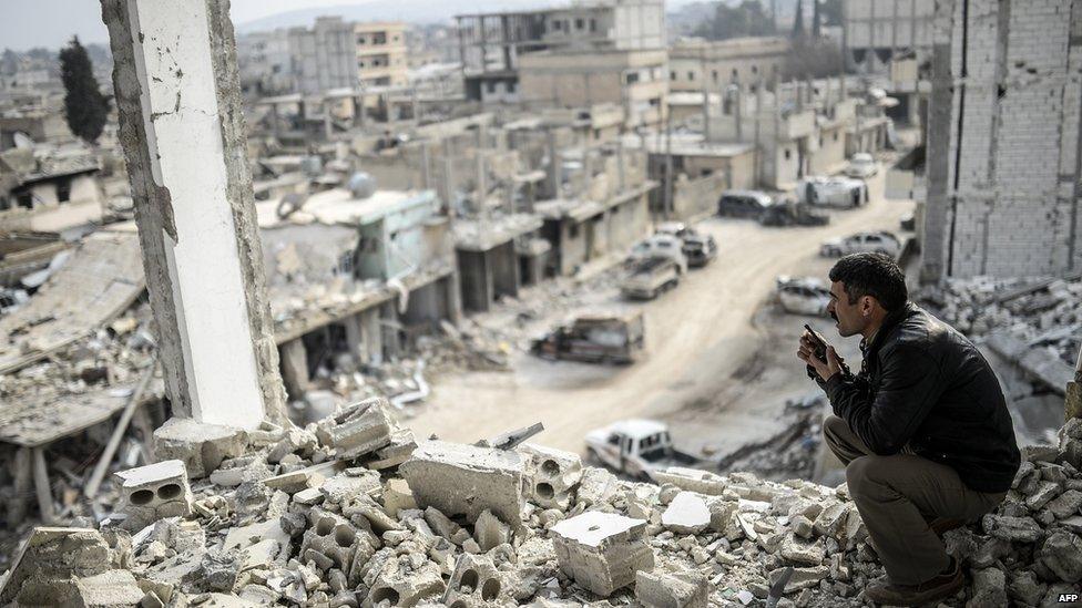 A Kurdish man talks with a radio as he checks the eastern part of the Syrian border town of Kobane, known as Ain al-Arab, on 28 January 2015