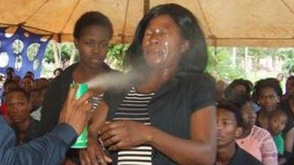 A man spraying insecticide in the face of a woman before a congragation.