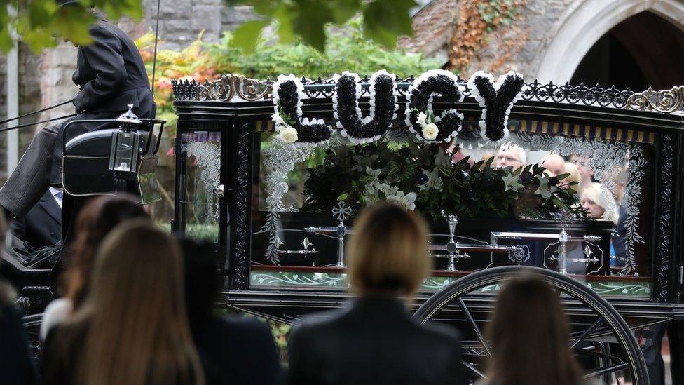 "Lucy" written in flowers above the horse-drawn carriage carrying her coffin