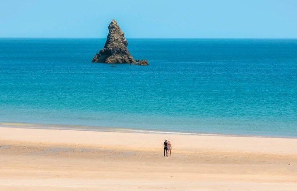 A rock stands out of a deep blue sea on a clear sky