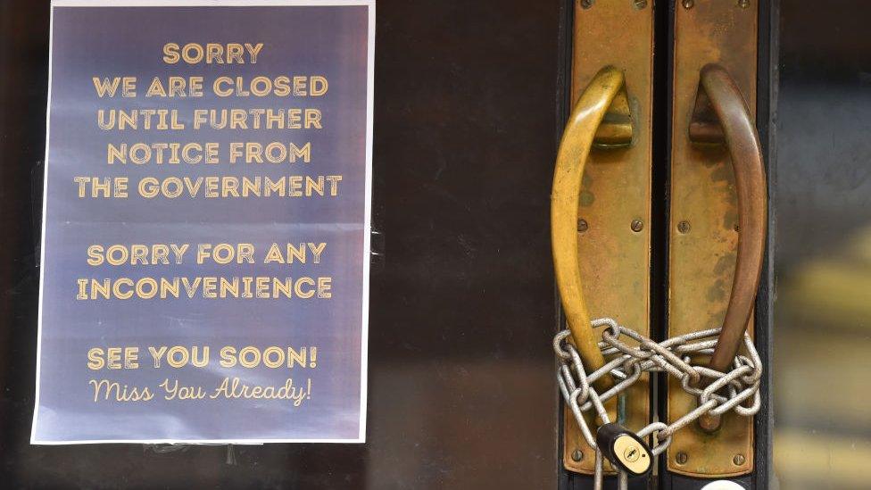 A locked shop displays a sign saying 'sorry we are closed until further notice from the Government, sorry for any inconvenience, see you soon