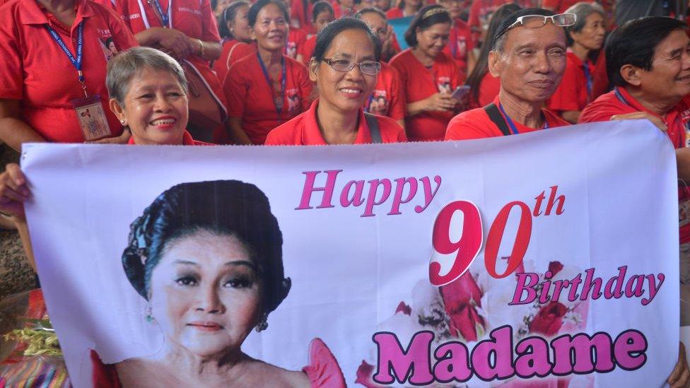 Supporters dressed in red hold up a "Happy 90th Birthday Madame" banner