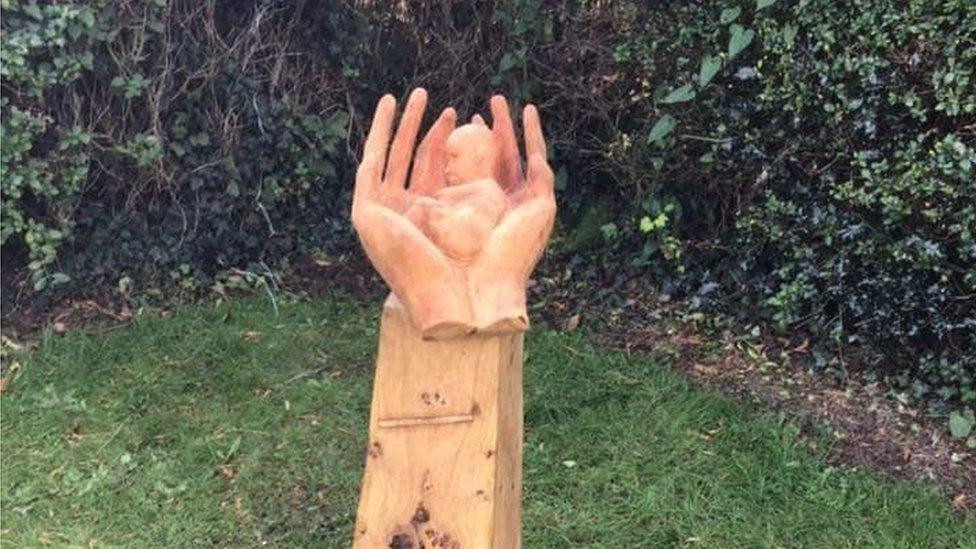 Memorial sculpture of a baby cradled in a pair of hands