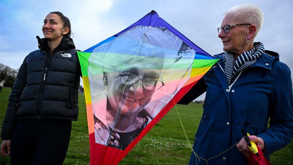 Two woman hold a kite with the face of a Covid-19 victim on it in Bristol