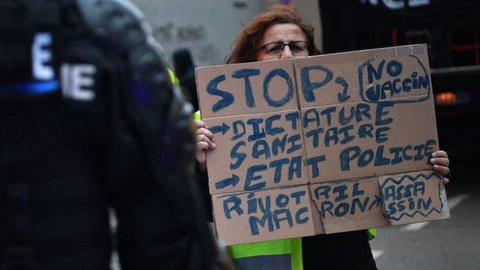 Protester holding an anti-vaccine sign in front of gendarmes.