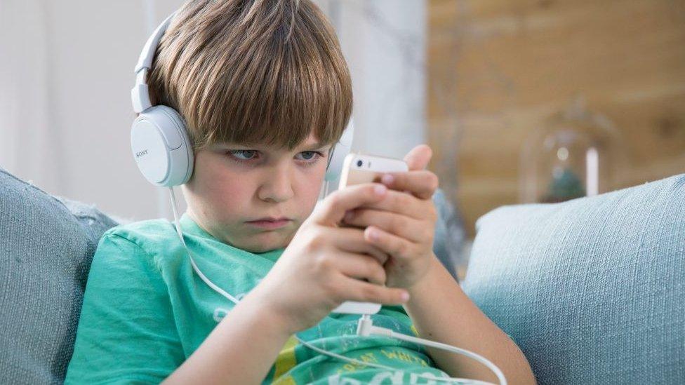 A boy with headphones on looks at his mobile phone