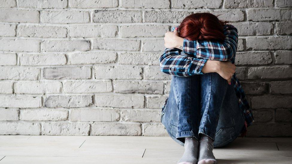 Domestic abuse - women with head in arms sitting against a wall