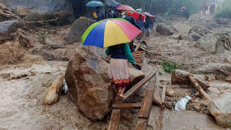 People walk across a makeshift bridge over flood water in Blantyre