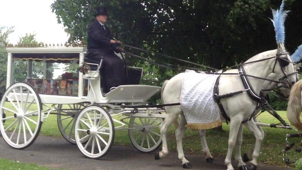 coffin in carriage, which is pulled by white horses