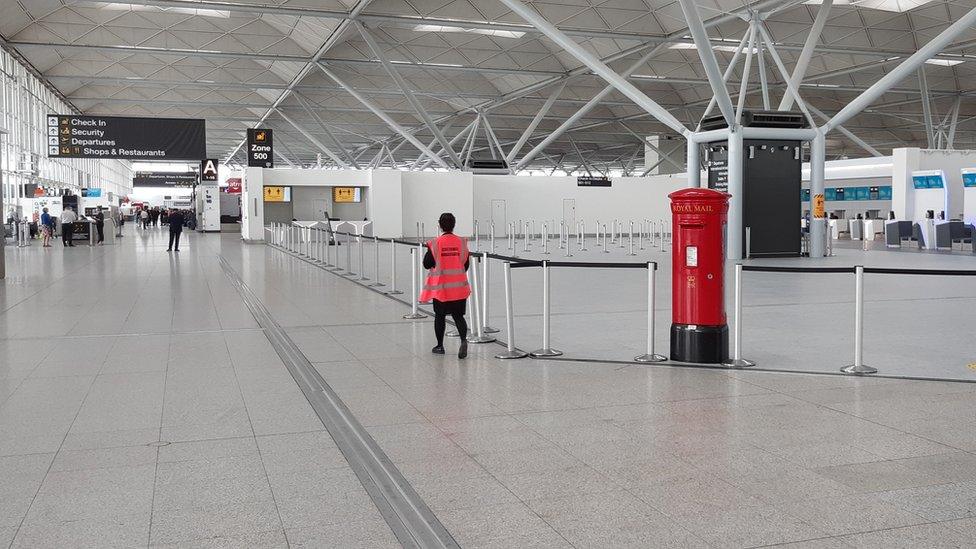 Large white terminal building, showing red pillar box, direction signs and staff member in red hi-viz jacket.