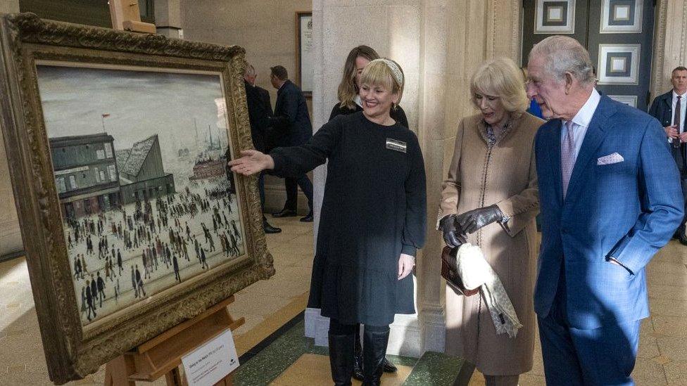 King Charles III and the Queen Consort views L.S. Lowry's "Going to the Match" painting during a visit to Bolton Town Hall