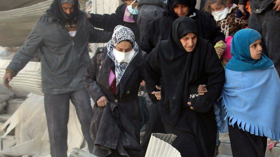 Syrians walk through rubble of damaged buildings as they flee clashes between government forces and rebels in Aleppo, Syria (28 November 2016)